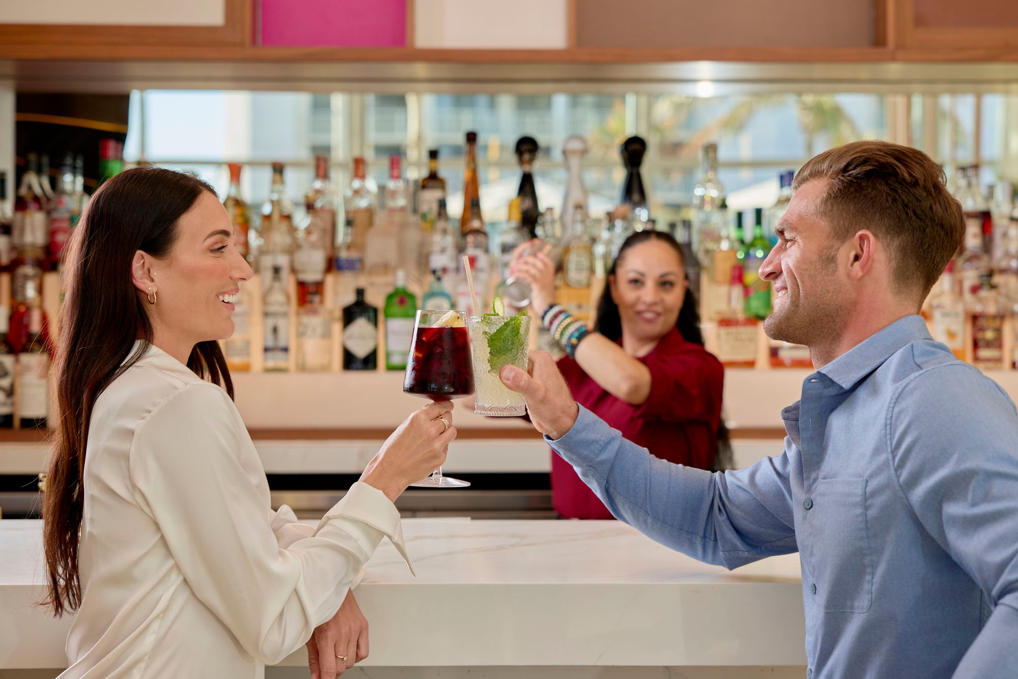 A man and a woman sitting at the bar smiling at each other with cocktails in their hands at Lala