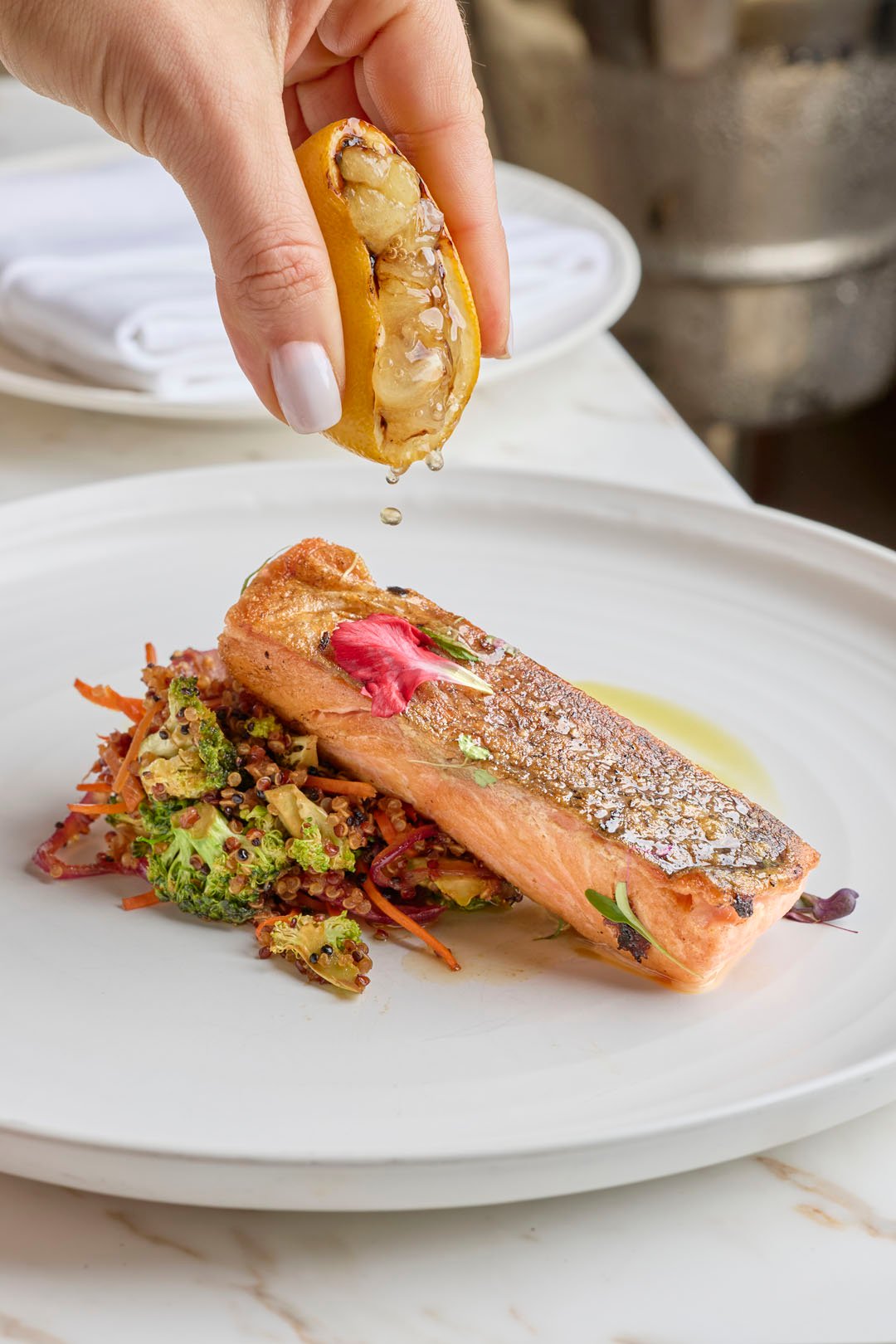 A Salmon dish with charred lemon being squeezed on top of the salmon on a circular white plate at Tula