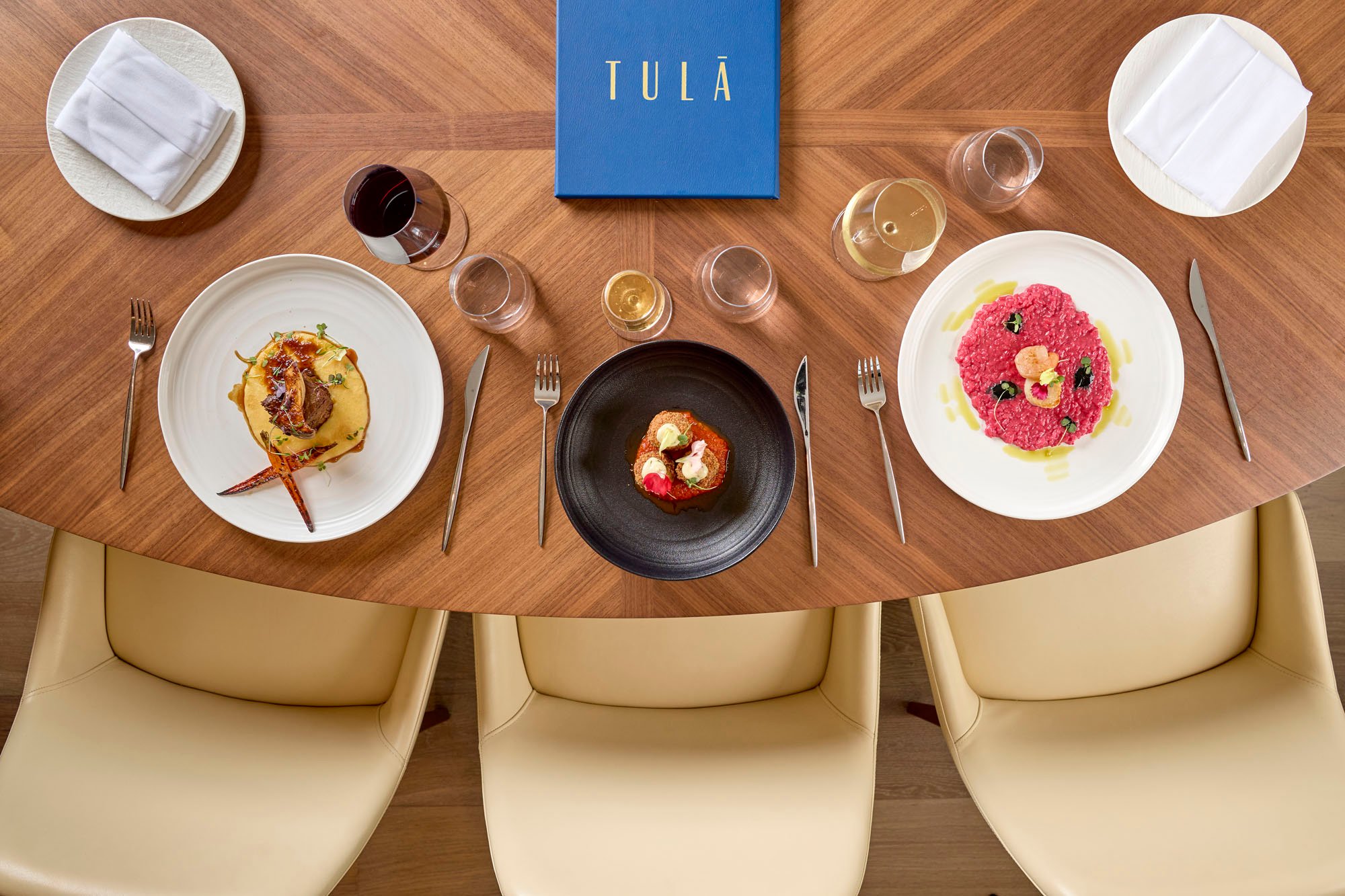 A spread of 3 dishes on a wooden table with wine pairings at Tula