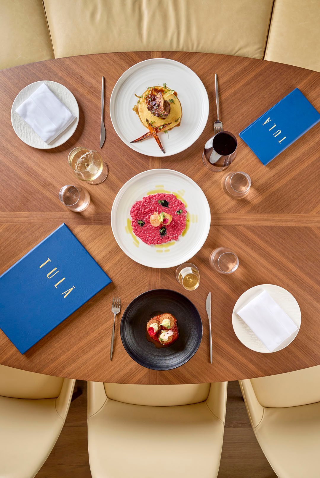 A spread of 3 dishes on a wooden table with wine pairings at Tula