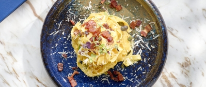 A beautiful pasta dish with micro greens in a circular black bowl at Tula