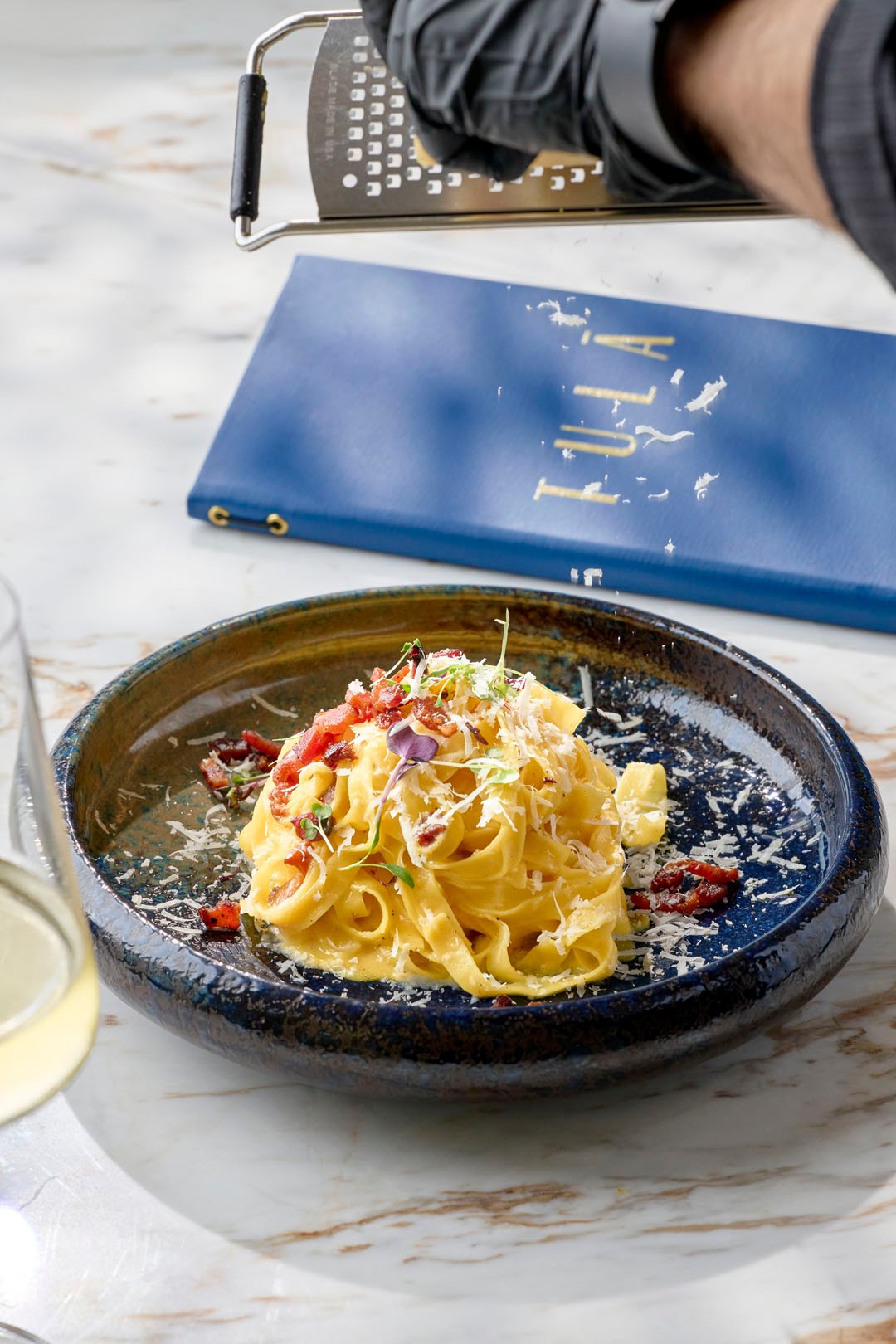 A beautiful pasta dish with micro greens in a circular black bowl at Tula