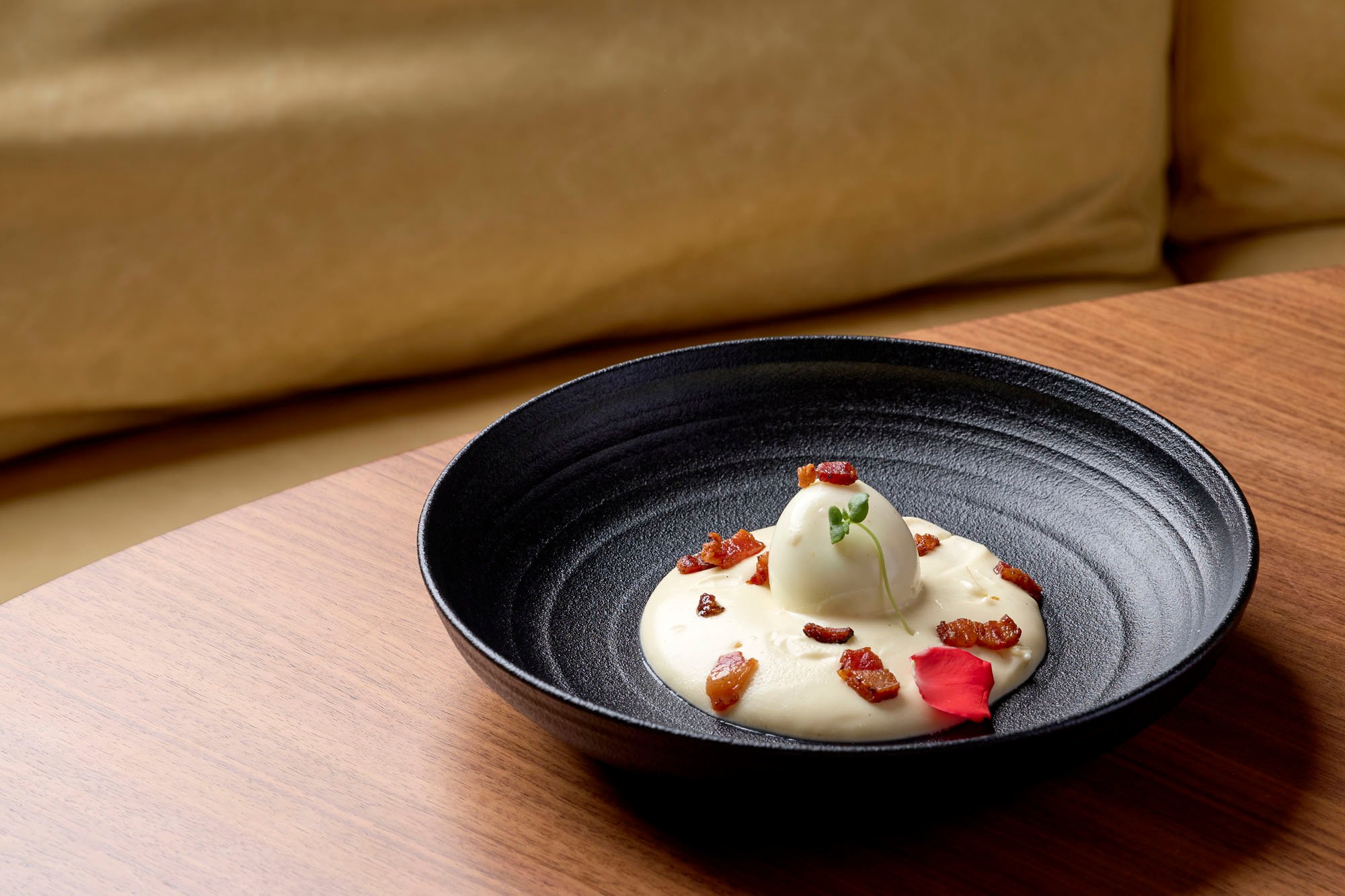 An egg covered in a cream sauce and bacon bits at Tula