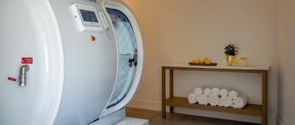 A hyperbaric chamber next to a table of white towels, citrus and spa water.