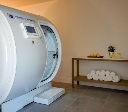 A hyperbaric chamber next to a table of white towels, citrus and spa water.
