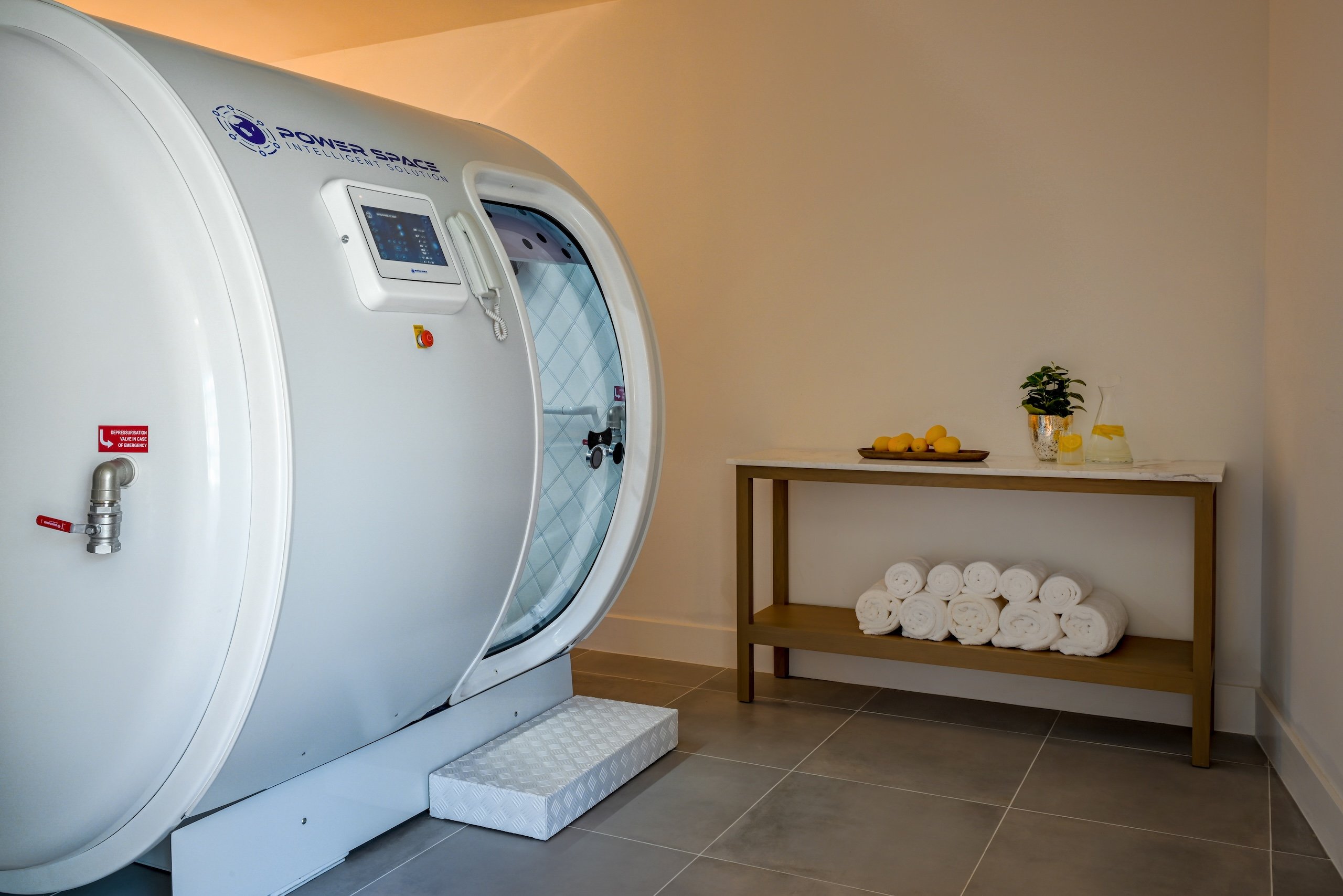 A hyperbaric chamber next to a table of white towels, citrus and spa water.