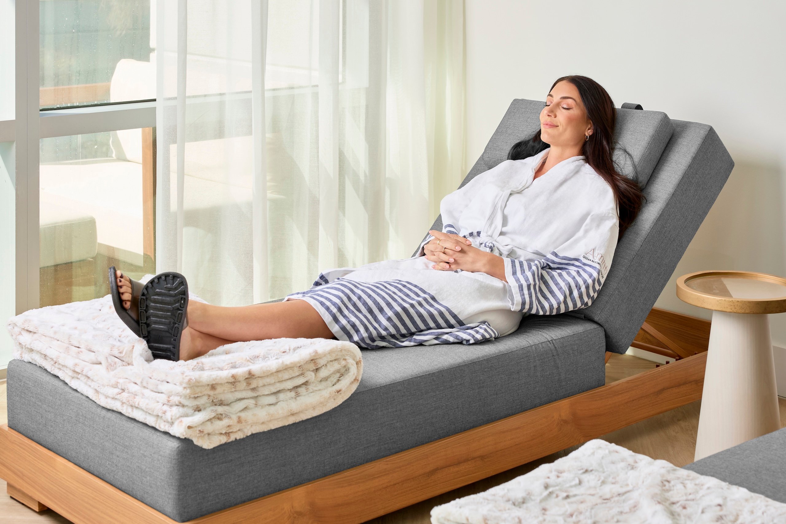 A woman wearing a robe lounges on a couch at Amrit Ocean Resort Wellness Spa, embodying relaxation and serenity.