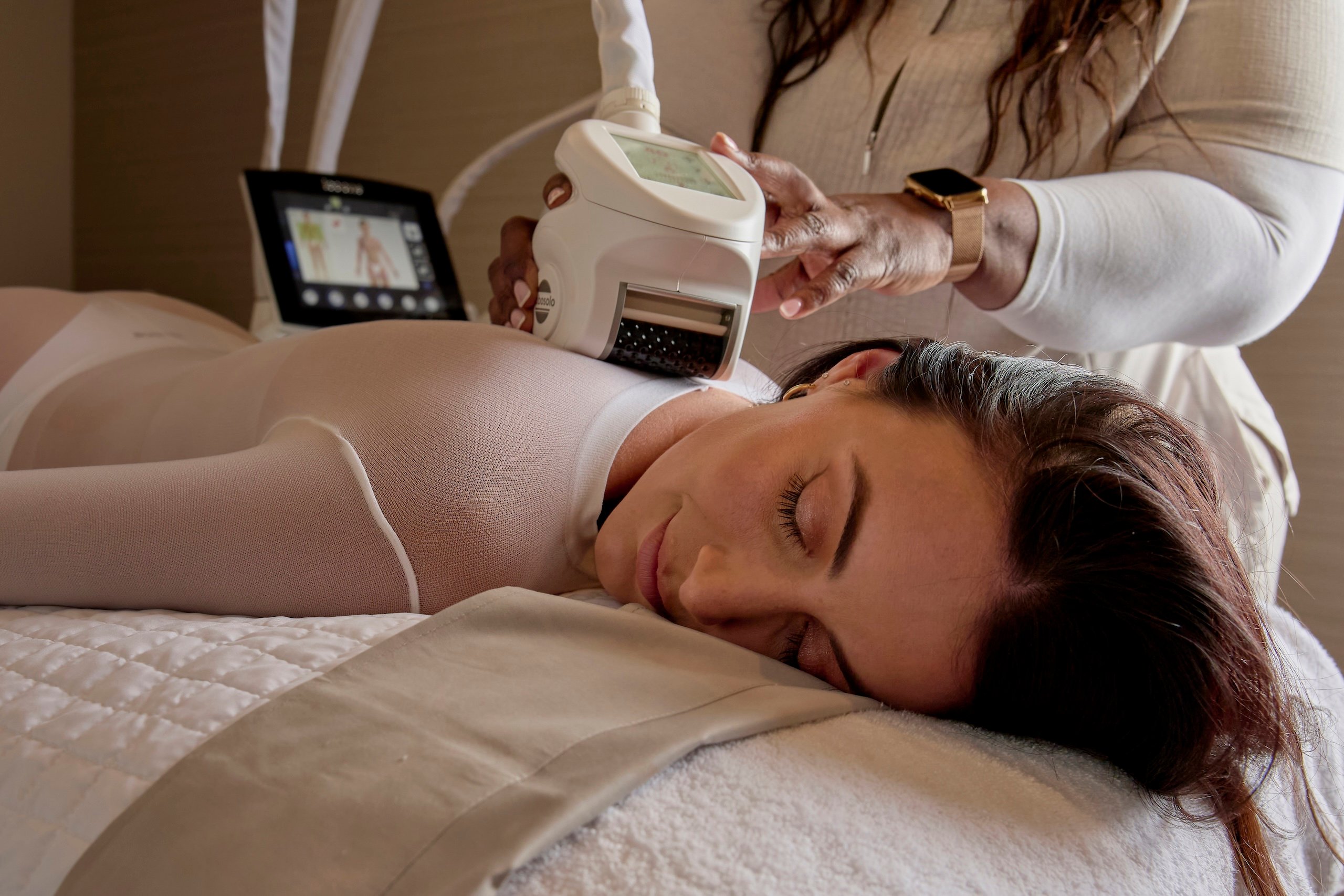 A woman lying on a bed as a therapist operates a massage machine, enjoying a treatment at Amrit Ocean Resort Wellness Spa.