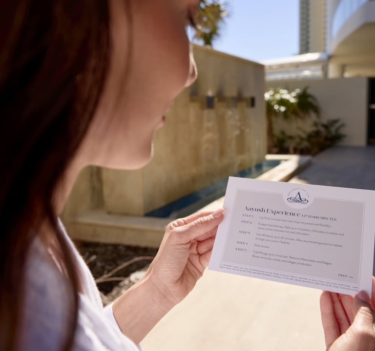 A woman reading a guide on the Aayush Hydrothermal experience from the Amrit Ocean Resort Spa