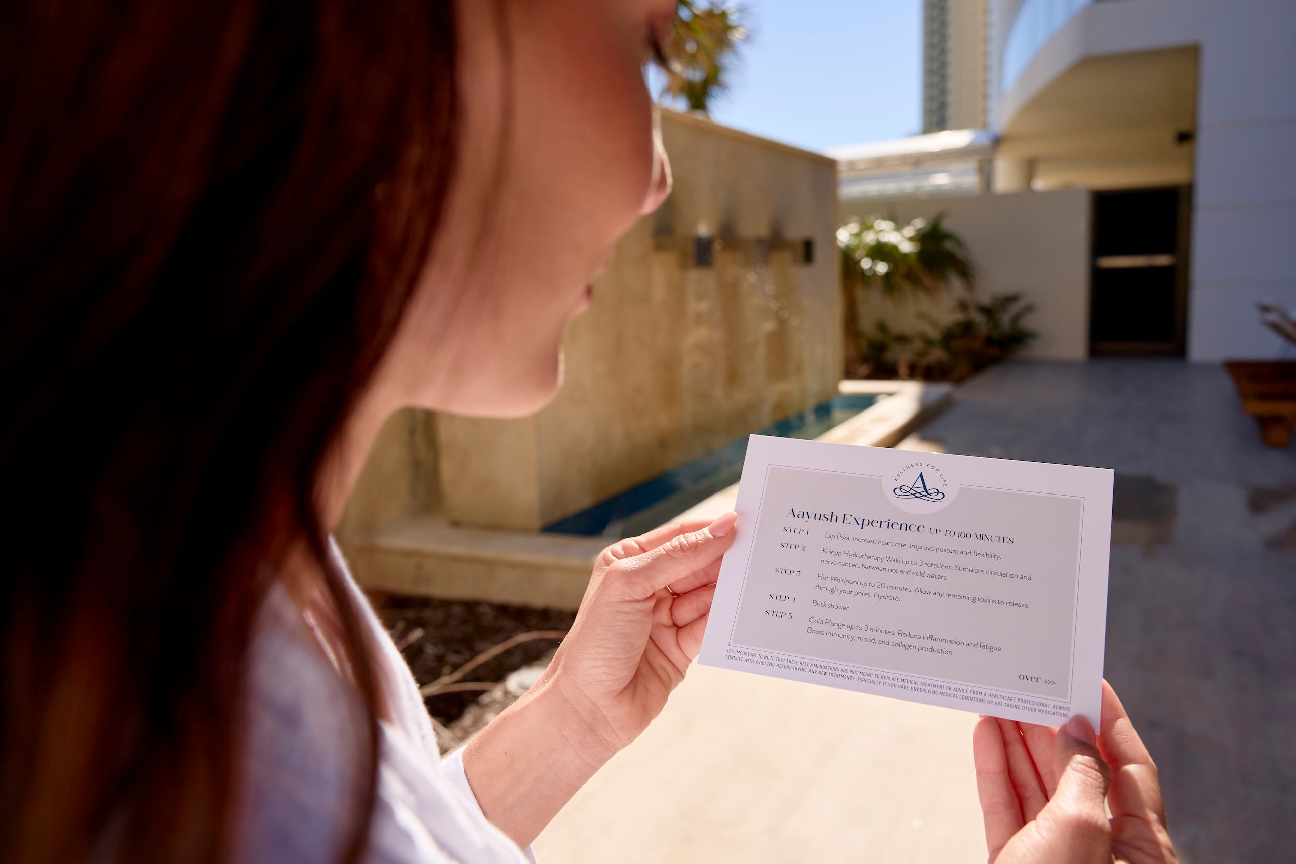 A woman reading a guide on the Aayush Hydrothermal experience from the Amrit Ocean Resort Spa