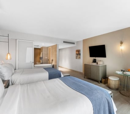 Two Queen beds, a table and a sitting area and a view of a soaker tub in an ocean view two queens room at the Amrit Ocean Resort