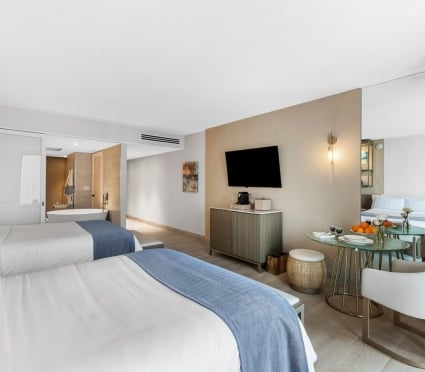 Two Queen beds, a table and a sitting area and a view of a soaker tub in an ocean view two queens room at the Amrit Ocean Resort